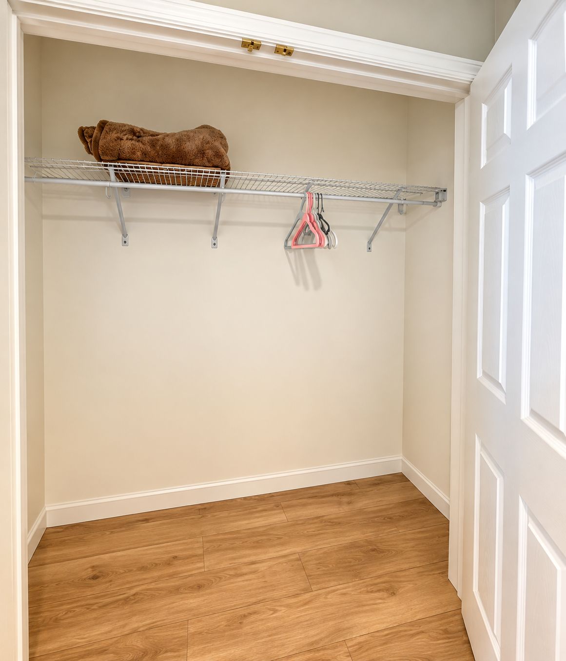 A closet with a metal shelf, a hanging rack, and a wooden floor.