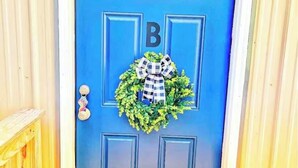 Uma porta azul com um letreiro com a letra 'B', uma grinalda e uma pequena janela acima da porta.