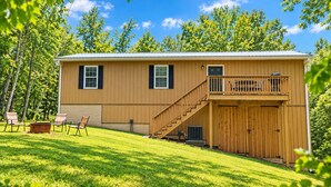Une maison en bois à deux étages, dotée d’un balcon, d’un porche couvert et d’un espace aménagé pour faire un feu de camp.