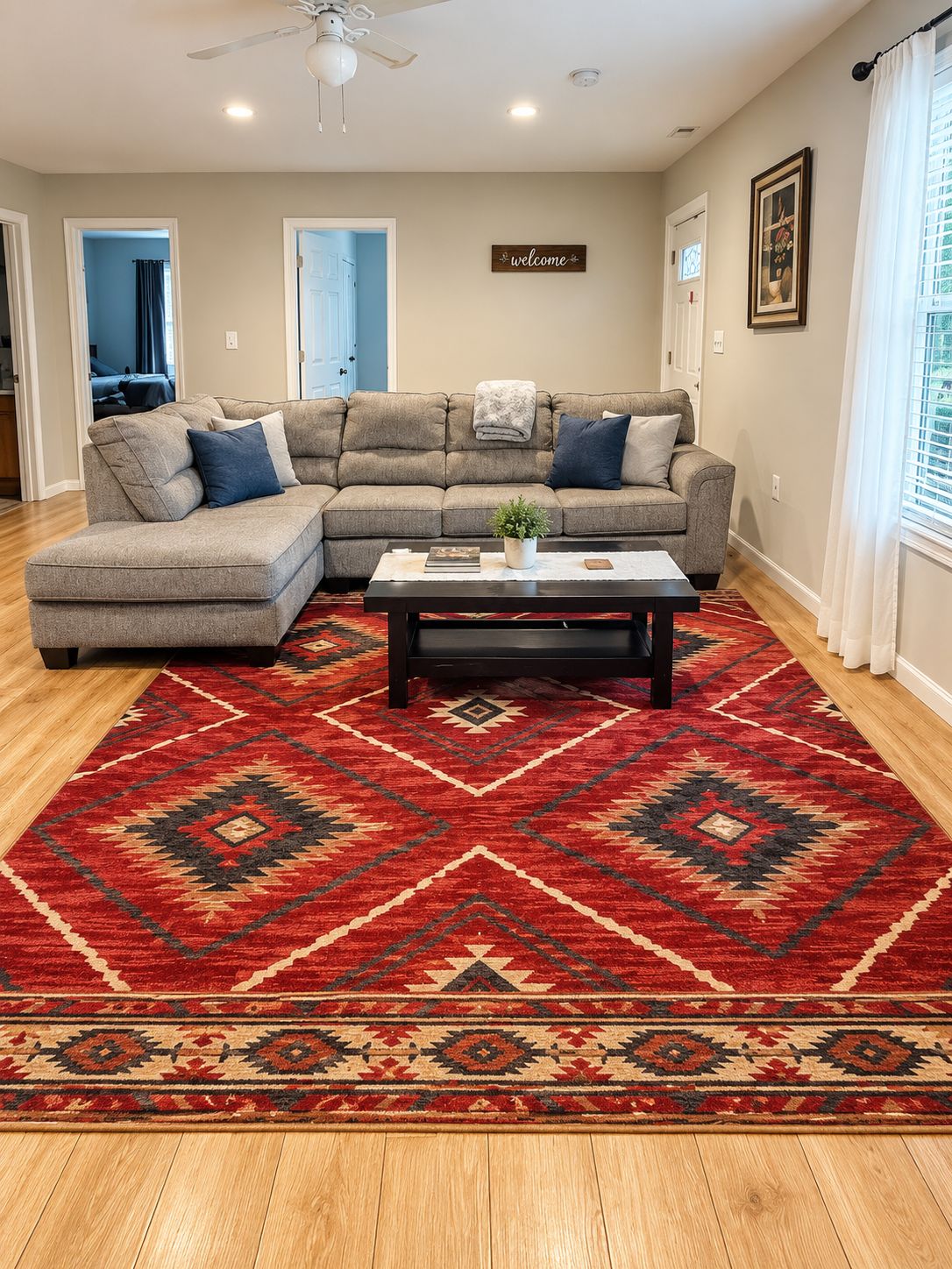 A living room with a sectional sofa, a coffee table, and a red patterned rug.