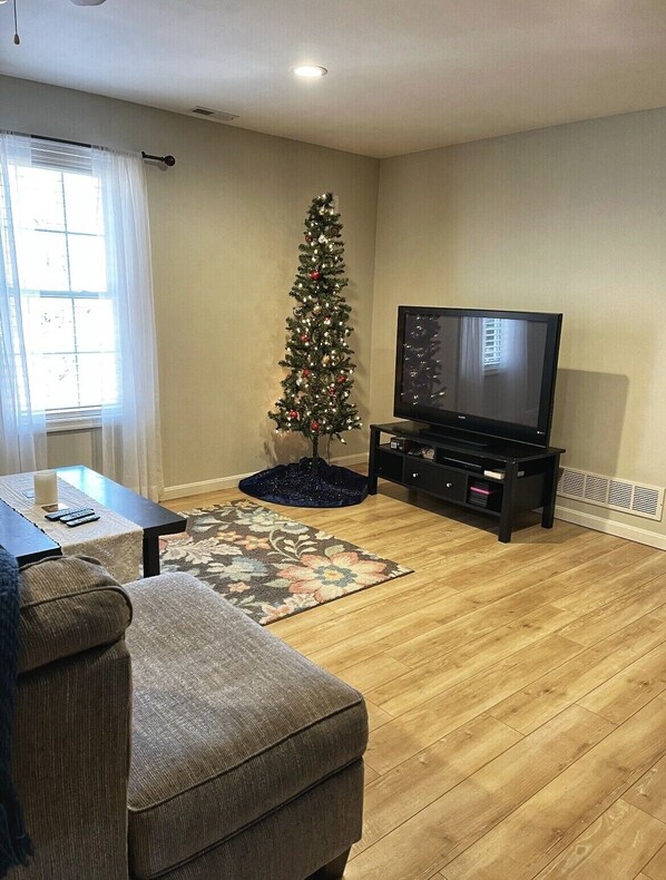 A living room with a wooden floor, a television, a Christmas tree, a sofa, and a coffee table.
