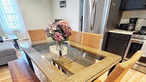 Uma cozinha moderna com uma mesa de jantar de vidro, cadeiras de vime, uma geladeira de aço inoxidável e uma cafeteira.