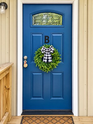 A blue door with a 'B' sign, a wreath with a bow, and a doormat.
