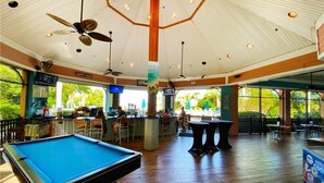 A pool table in a room with a high ceiling, wooden flooring, and a bar area with a 'Happy Hour' sign. - Amazing Bahama Bay Resort, close to Disney (Davenport)