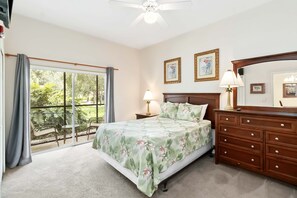 Relax in this serene bedroom with a large bed, dresser, and nightstand, offering a peaceful retreat with a view of lush greenery.