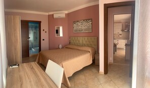 A bedroom with a bed, bedside table, and a view of a bathroom and kitchen.