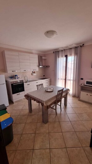 A kitchen with a dining table, cabinets, and a window with curtains.