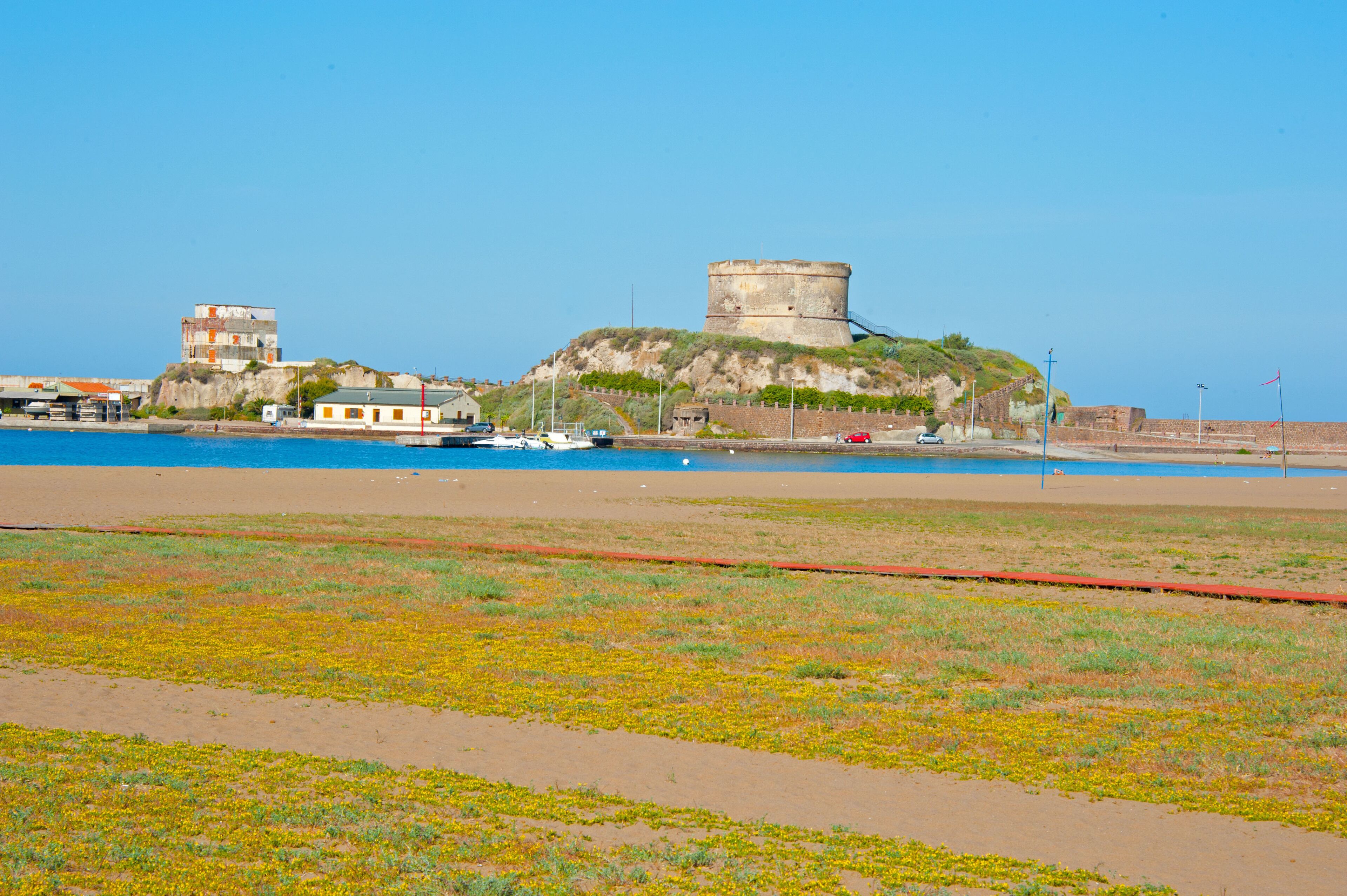 A coastal area with a fort on a hill, a beach, and a body of water.