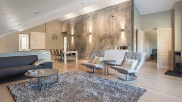 A spacious living area with a high ceiling, a dining table, two armchairs, a sofa, and a coffee table.