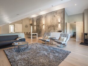 A spacious living area with a high ceiling, a dining table, two armchairs, a sofa, and a coffee table.