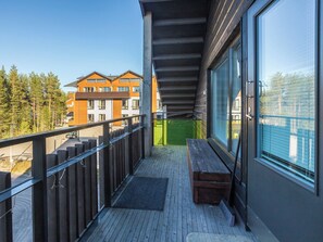 A balcony with a wooden floor, a bench, and a view of buildings and trees.