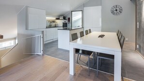A modern kitchen with white cabinets, a microwave, and a sink. There is a dining area with a white table and chairs.