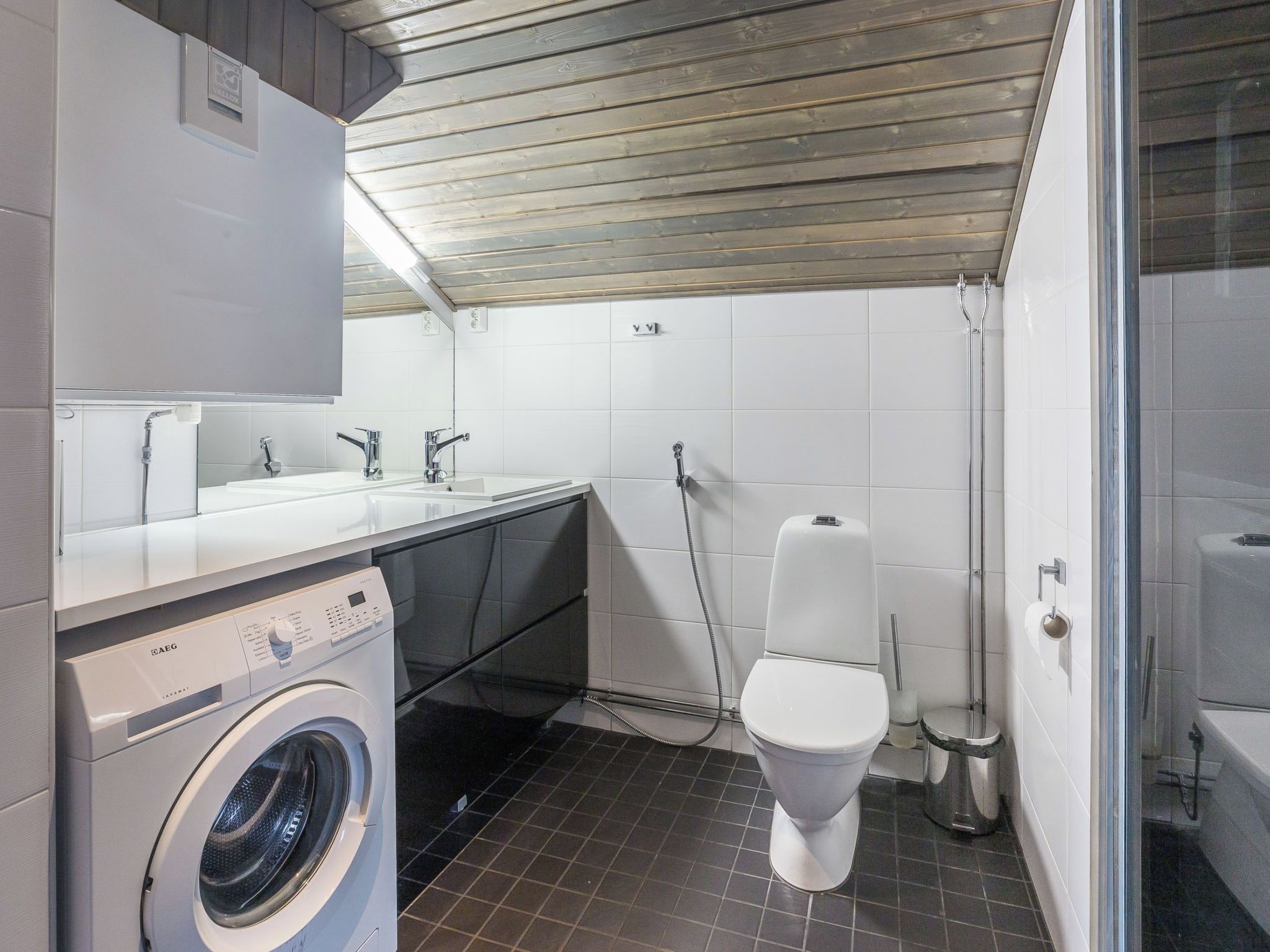 A compact, modern bathroom with a built-in washing machine, a toilet, and a shower area.