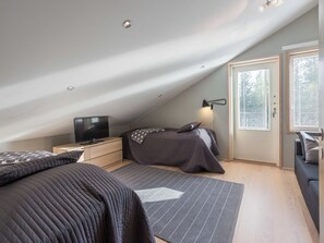 A bedroom with a sloped ceiling, a bed, a bedside table with a TV, a lamp, and a window with blinds. - Levin stara c 15 by Interhome (Kittilä)