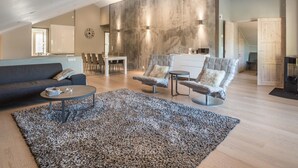 A spacious living area with a high ceiling, a dining table with chairs, a sofa, and two armchairs.