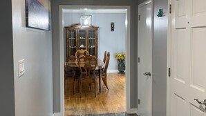 Un pasillo que conduce a un comedor con una mesa y sillas de madera, un armario con puertas de cristal y un jarrón con flores.
