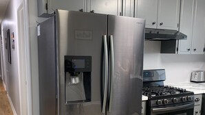 Un refrigerador de acero inoxidable con dispensador de agua, una estufa y un microondas en una cocina con gabinetes grises y piso de madera.