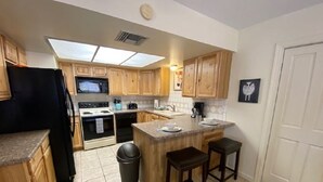 Una cocina con armarios de madera, un refrigerador negro, una estufa y un lavaplatos. Hay dos taburetes en la isla.