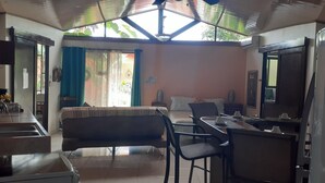 Une pièce comprenant un canapé, une table à manger, des chaises, un petit coin cuisine avec un évier et une grande fenêtre laissant entrer la lumière naturelle.
