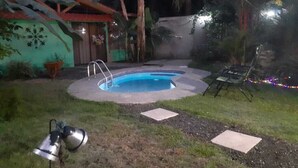 Une piscine dotée d’une terrasse en bois, entourée d’un jardin planté de palmiers et d’une maison avec un mur végétal.