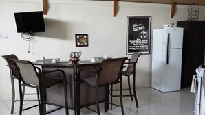 Un coin repas avec une table et des chaises, un téléviseur fixé au mur, un réfrigérateur et une affiche accrochée au mur.