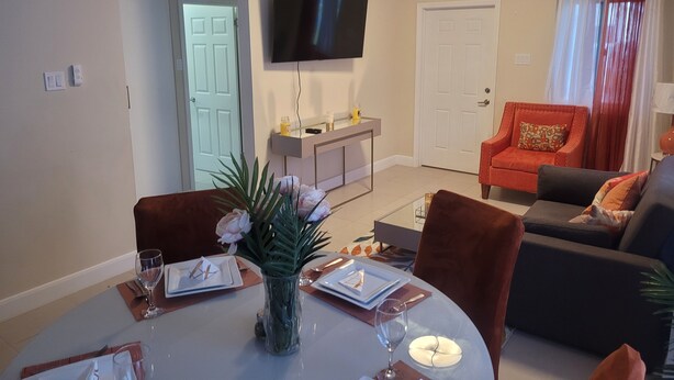 Un comedor con una mesa redonda preparada para dos personas, un jarrón con flores y un televisor de pantalla plana montado en la pared.