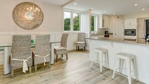 A modern kitchen with white cabinetry, a large island with bar stools, and a hanging light fixture. - Oceanfront, Spacious, Dog-Friendly Shipwatch Condo with Heated Pool (Fernandina Beach)