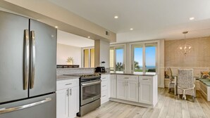 A modern kitchen with stainless steel appliances, white cabinetry, and a view of the ocean. - Oceanfront, Spacious, Dog-Friendly Shipwatch Condo with Heated Pool (Fernandina Beach)
