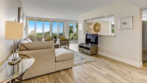 A modern living room with a beige sofa, a glass coffee table, and a TV stand. - Oceanfront, Spacious, Dog-Friendly Shipwatch Condo with Heated Pool (Fernandina Beach)