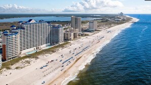 Un hotel costero con varios edificios altos, una playa con sombrillas y una vista del océano y un puente a lo lejos.