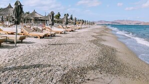 Una playa con tumbonas y sombrillas, cielo despejado y mar tranquilo.