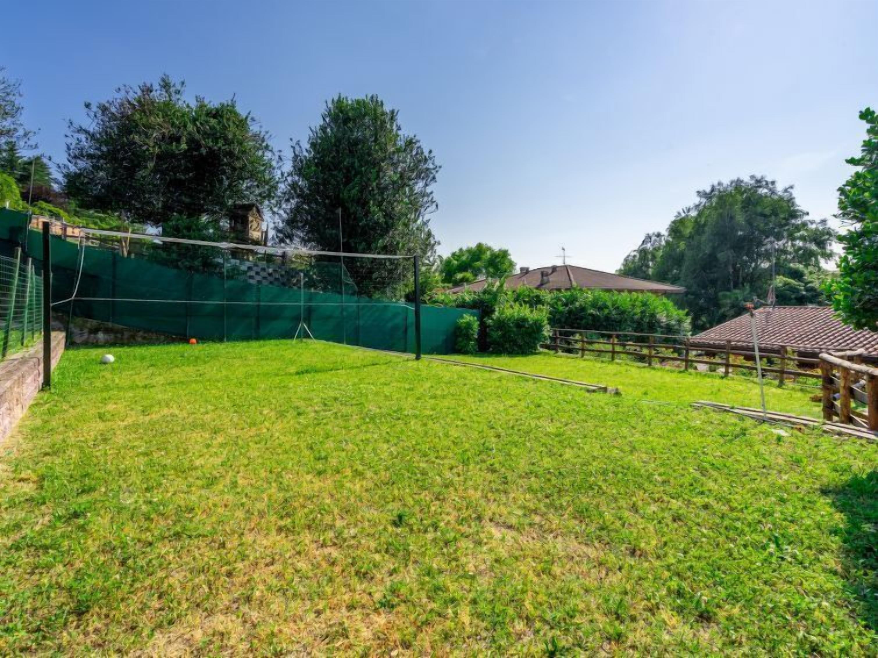 A grassy outdoor area with a volleyball net, a small wooden structure, and a fenced area.
