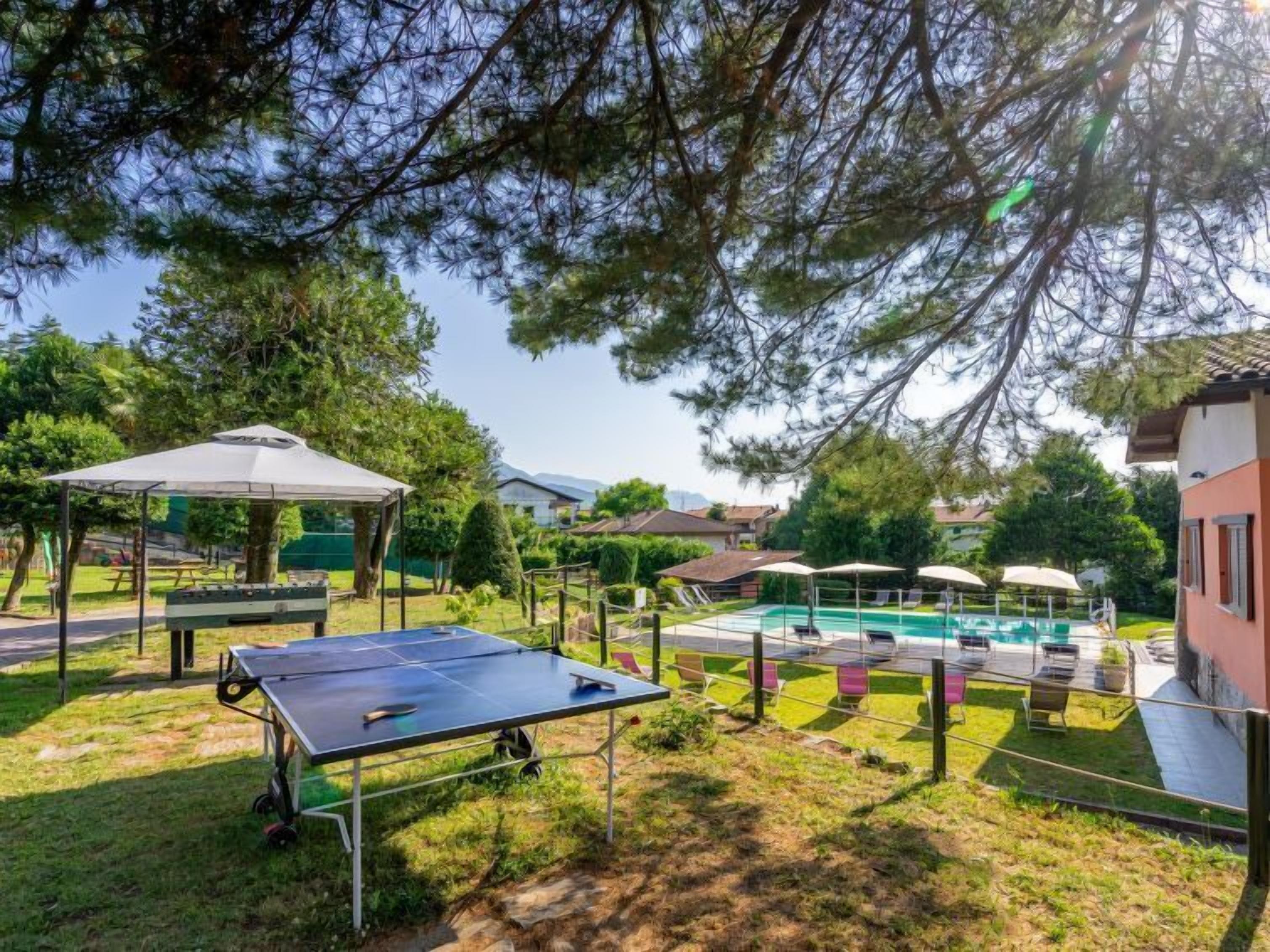 Ett utomhusområde med ett bordtennisbord, en möblerad sittplats under tak och en swimmingpool.