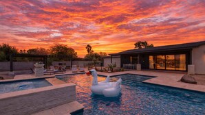 Une piscine avec un flotteur en forme de cygne, des chaises longues et un espace patio au coucher du soleil.