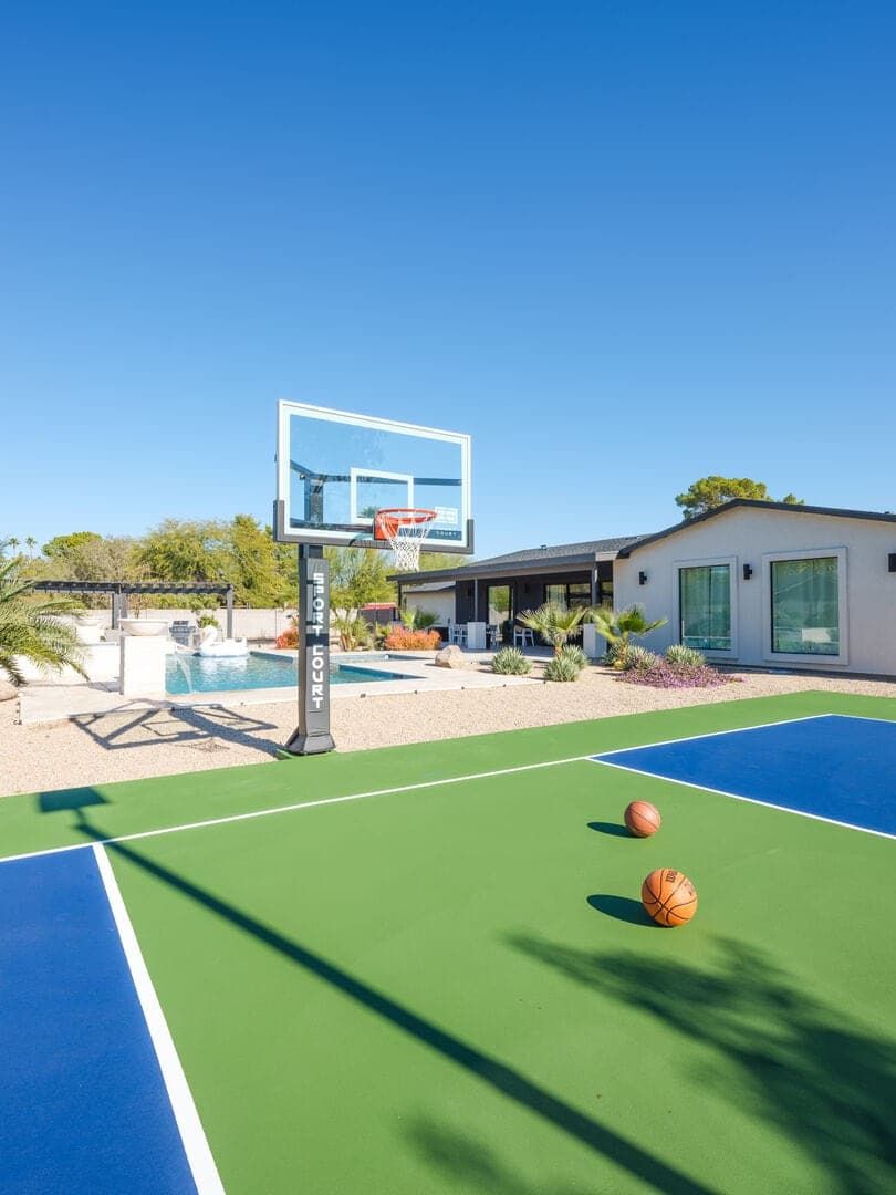 Una cancha de baloncesto al aire libre con una piscina y una casa al fondo.