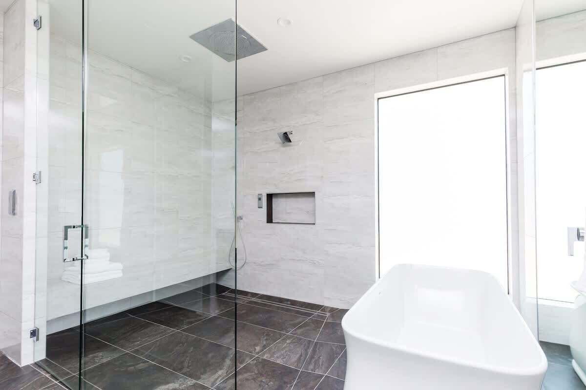 A modern bathroom with a glass shower enclosure, a white bathtub, and a tiled floor.