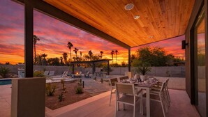 Une terrasse extérieure avec une piscine, des chaises longues et une table à manger pour deux personnes.