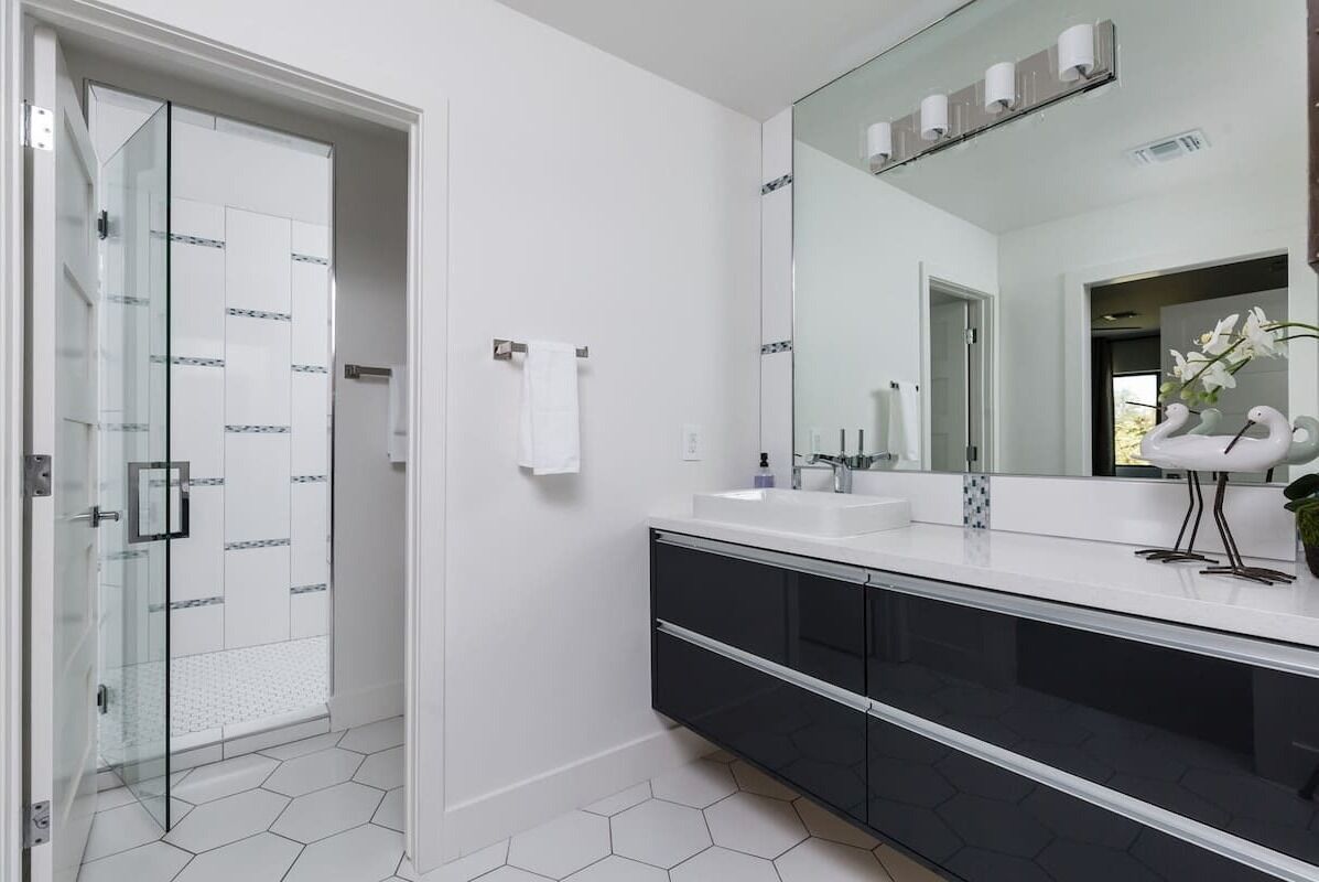 Une salle de bain moderne dotée d’une douche à parois de verre, d’un grand miroir et d’un meuble-lavabo noir avec un plan de travail blanc.