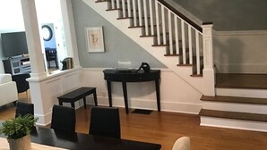 Un vaste salon comprenant un escalier, un coin repas et un téléviseur placé au fond de la pièce.
