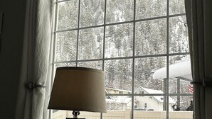 Une pièce avec une grande fenêtre, une lampe sur une table et une vue sur une forêt enneigée.