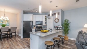 A modern kitchen with white cabinetry, a central island with stools, a refrigerator, microwave, and a coffee maker. - Gorgeous Clean 3 Bdrm, 2 Owner Suites, South Forest Beach, near beach and pool! (Hilton Head Island)