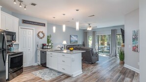 A modern kitchen with white cabinets, a central island, and a dining area with a gray sofa. - Gorgeous Clean 3 Bdrm, 2 Owner Suites, South Forest Beach, near beach and pool! (Hilton Head Island)