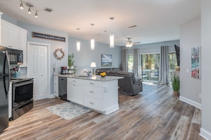 A modern kitchen with white cabinets, a central island, and a dining area with a gray sofa.