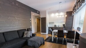 A modern living room with a dark sofa, a coffee table, and a dining area with a white table and chairs. - Tunturinlaita b3 by Interhome (Kittilä)