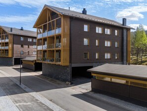 Ein modernes, mehrstöckiges Gebäude mit Balkonen, einer flachen Dachterrasse und blauem Himmel.