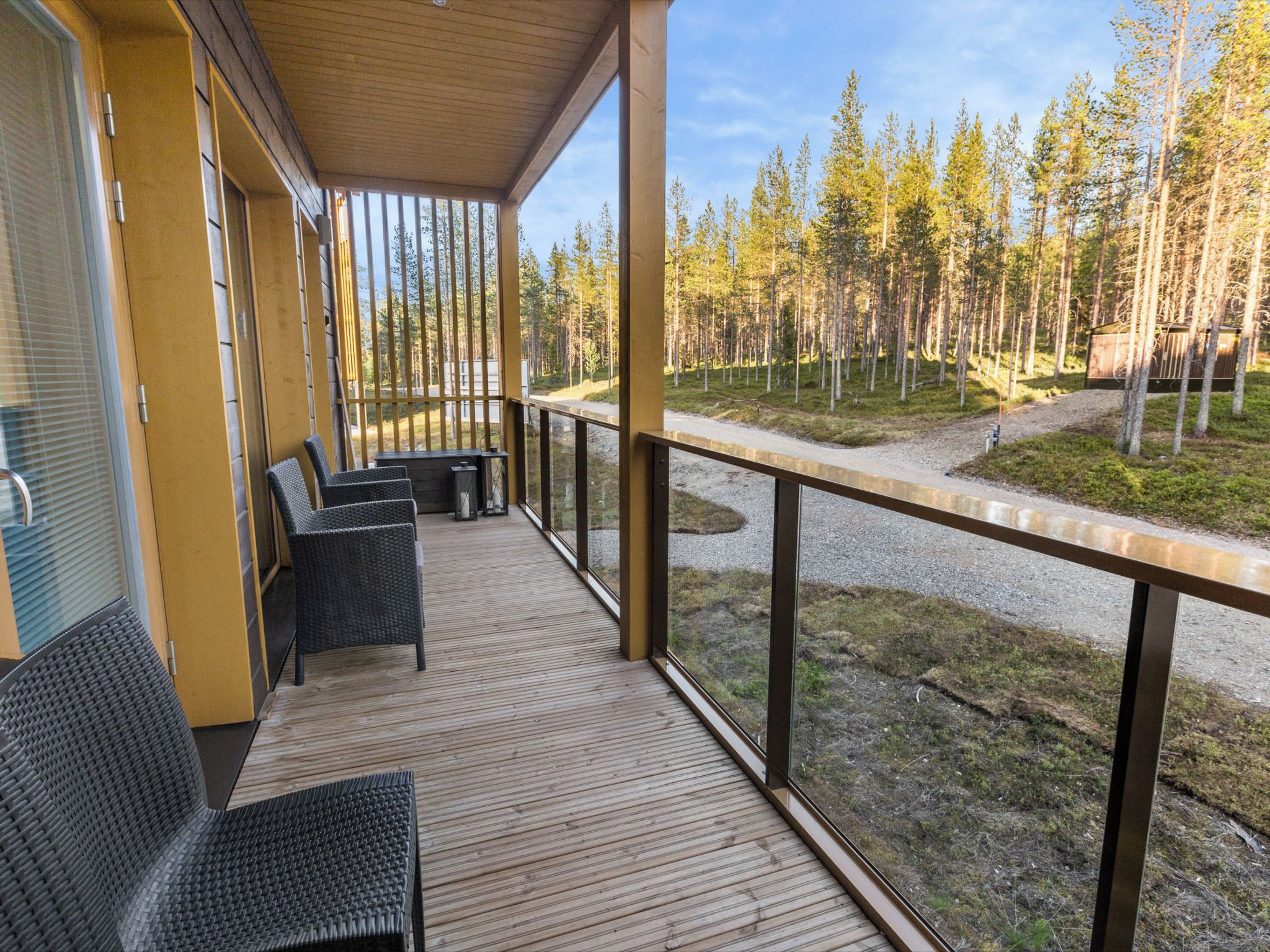 A covered outdoor area with wooden flooring, metal railings, and wicker furniture.