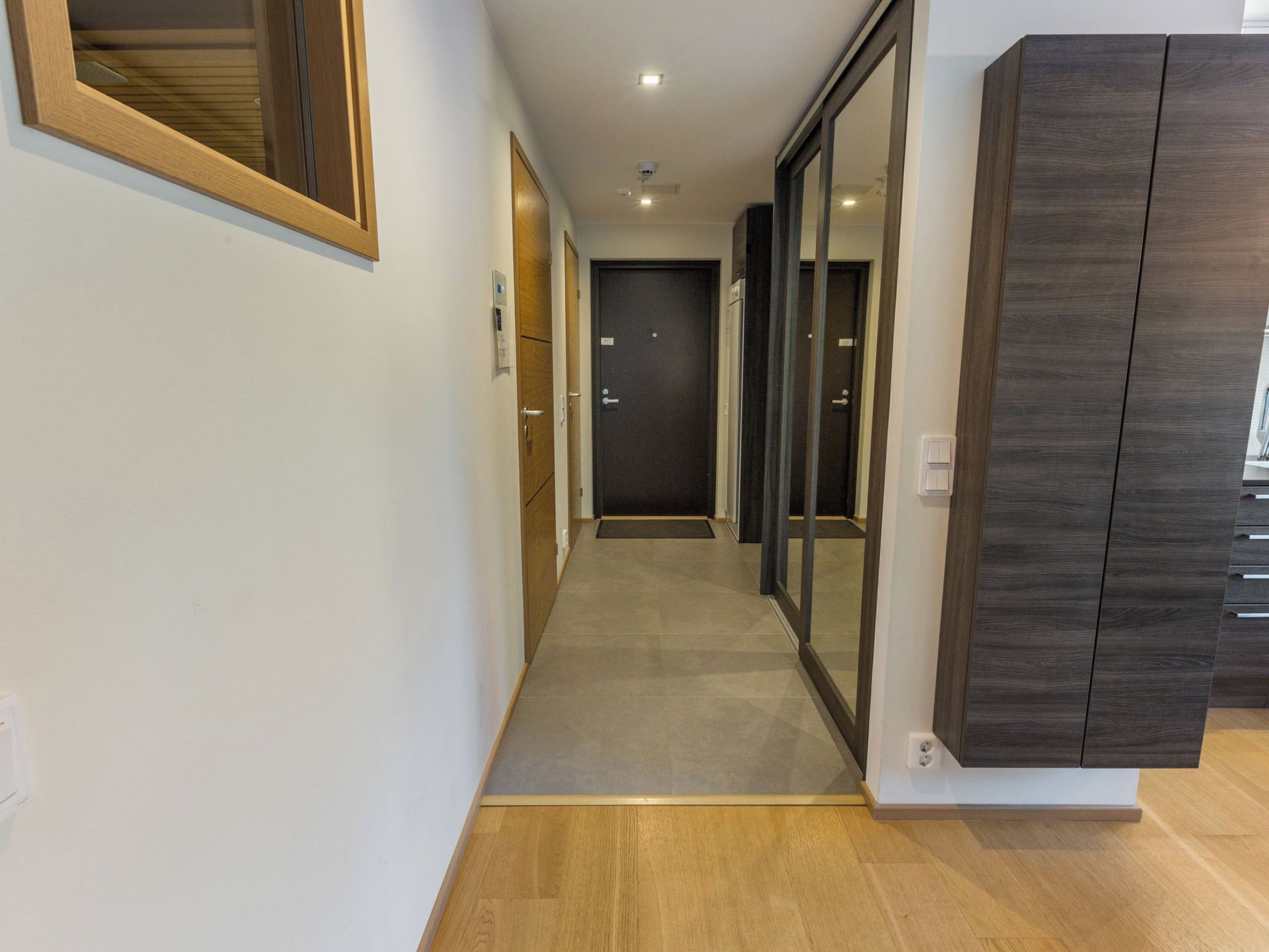 A hallway with a wooden floor, a door at the end, and a wall-mounted cabinet.