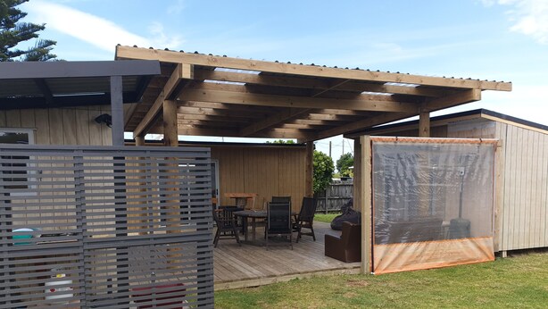 A covered patio area with a wooden deck, outdoor furniture, and a fenced play area. - Perfect in Pataua (Pataua North)
