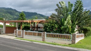 Zona residencial con porche cubierto, entrada protegida por un muro y abundante vegetación, entre ellas, plataneros.