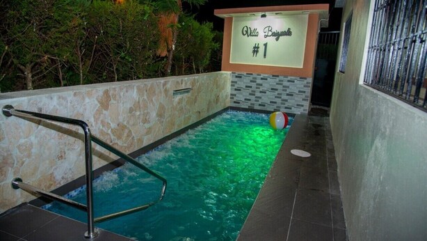 Una piscina con una escalera metálica, un cartel que dice "Villa Bajuns #1" y una pelota de playa en el borde.